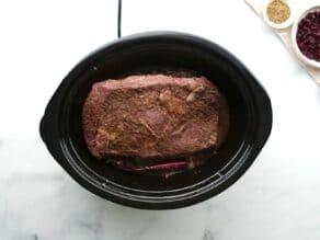 Cooked brisket in slow cooker crock pot, garnishes on the side.