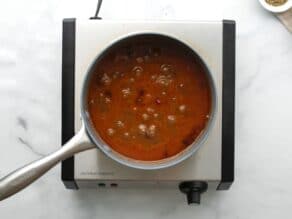 Pan of brisket sauce vegetable puree with cranberries simmering on stovetop.