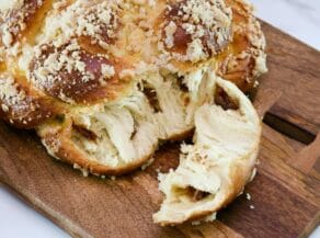 Baked Cinnamon Date Challah on wooden cutting board, a piece torn off to show the date filling, on a marble countertop.