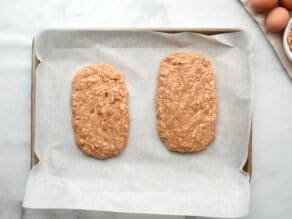 Horizontal overhead shot of a baking sheet lined with parchment paper. Two rectangles of raw mandel bread dough lay on top.