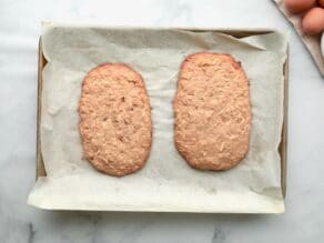 Horizontal overhead shot of a baking sheet lined with parchment paper. Two rectangles of baked mandel bread dough lay on top.