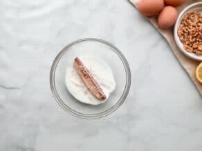 Horizontal overhead shot of a slice of mandel bread being dipped into a bowl of sugar.