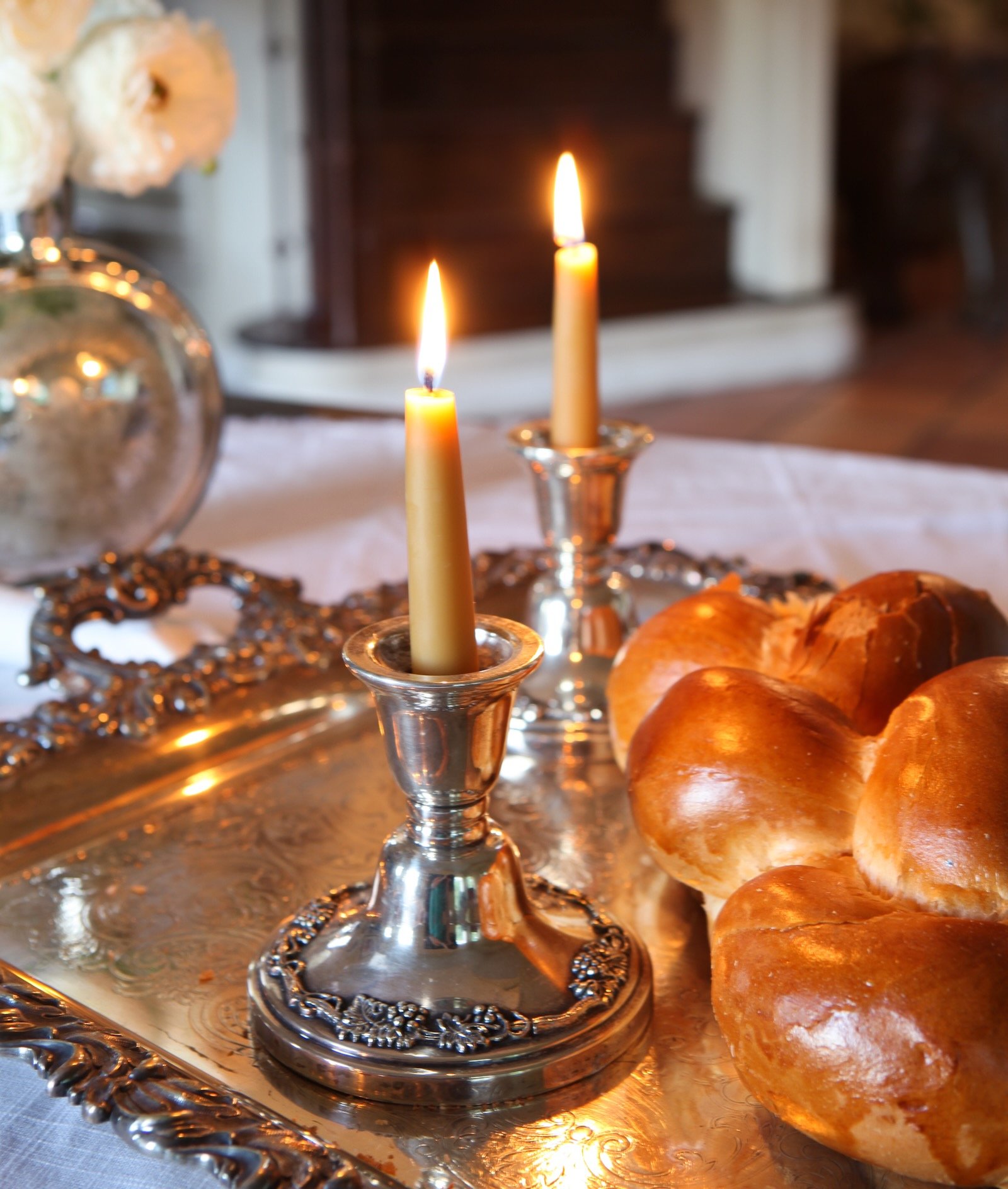 Two lit candles next to a Jewish bread on a fancy tray