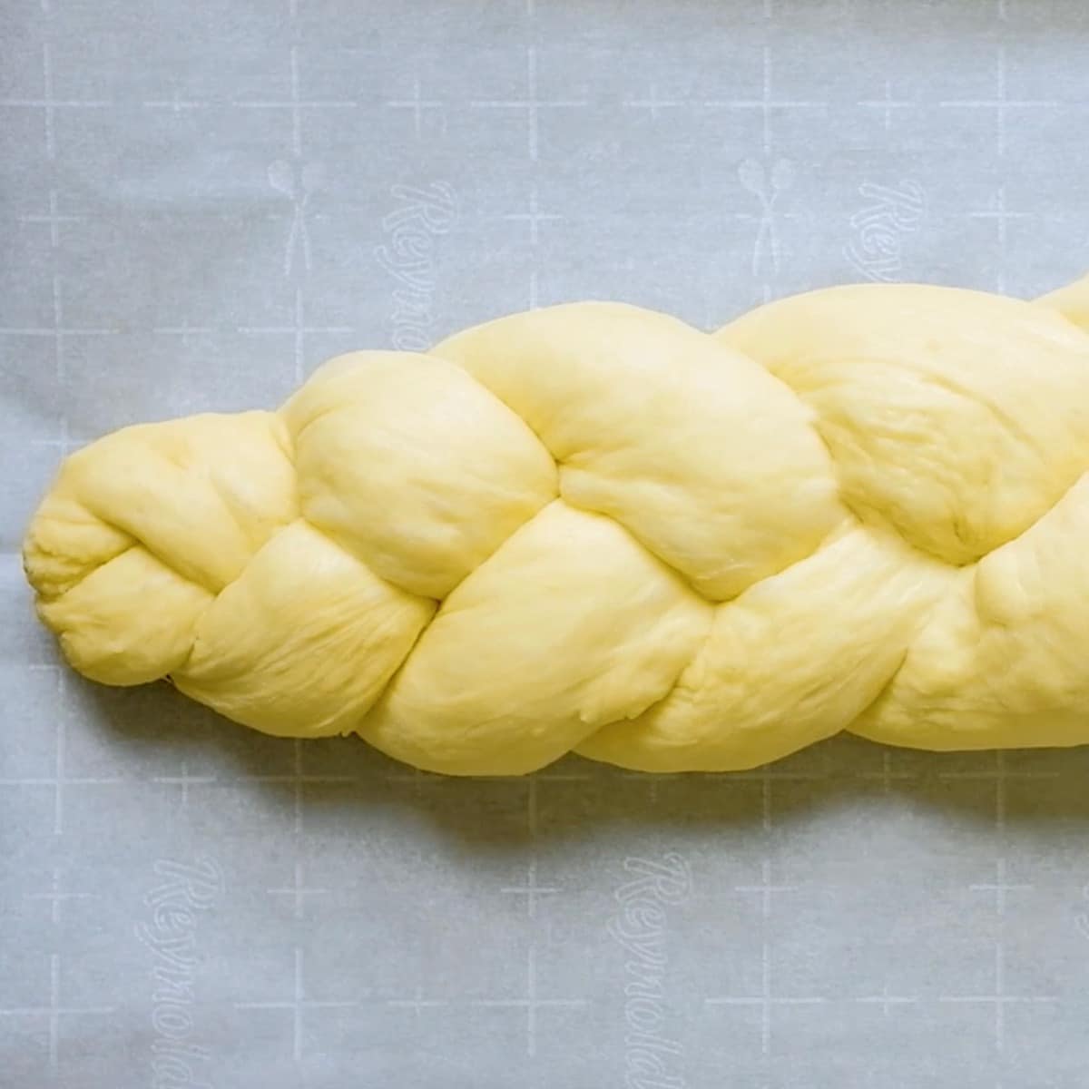 Square Crop picture of a Braided challah dough on parchment-lined baking sheet.