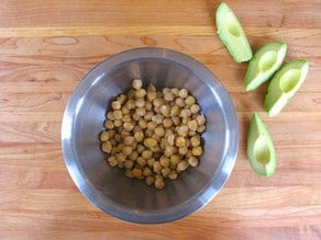 Sliced avocado next to a bowl of chickpeas.