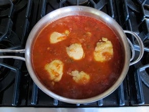 Fried chicken thighs in saucepan of tomato sauce.