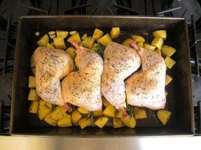 Chicken parts laid over potatoes in a roasting dish.