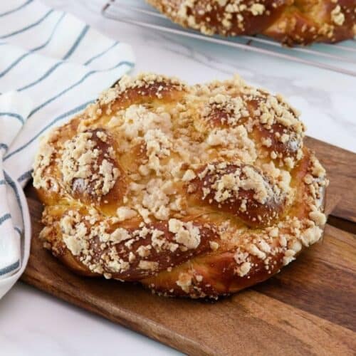 Horizontal shot of baked challah topped with a cinnamon crumble, sitting on a wooden cutting board.