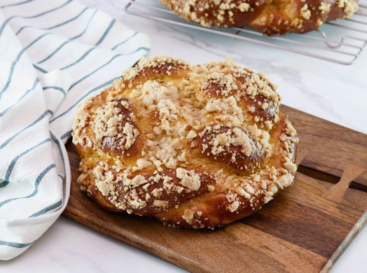 Horizontal shot of baked challah topped with a cinnamon crumble, sitting on a wooden cutting board.