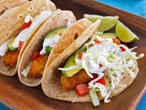 Close-up shot of crispy panko fish tacos with sliced lemon on the sides.