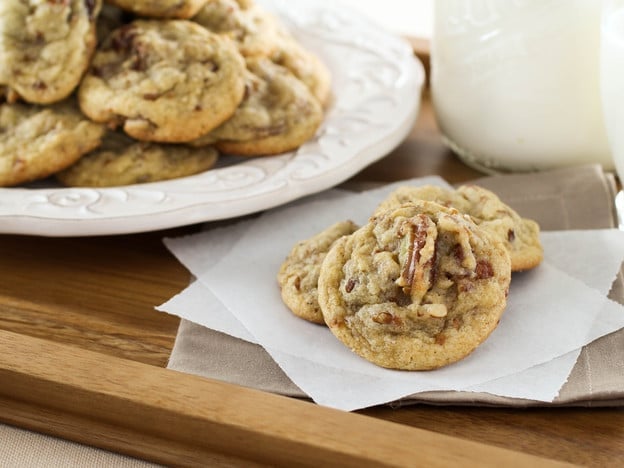 Date Cookies made of butter cookies with gooey dates and toasted pecans on a whiter plate and paper parchment papers