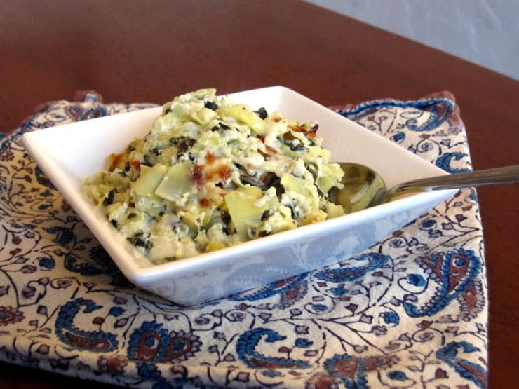 Spinach Artichoke Dip served on a square-shaped bowl with a spoon and on top of a table clothe