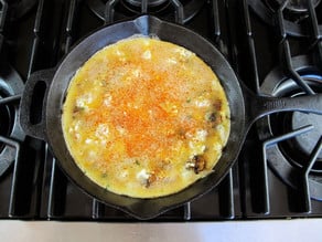 Eggs poured over mushrooms in a skillet.