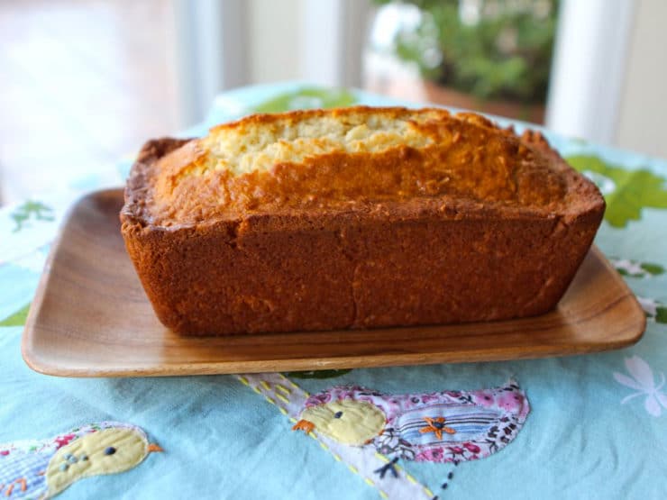 A golden-brown coconut cake sits on a brown, upward-curved plate, rests on a tablecloth adorned with a charming chick design.