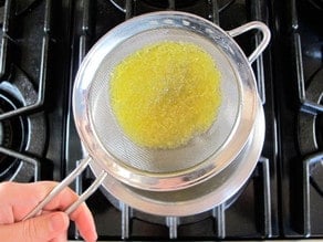 Straining ginger syrup on stovetop for ginger beer.