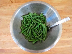 Tossing green beans with dressing in a bowl.