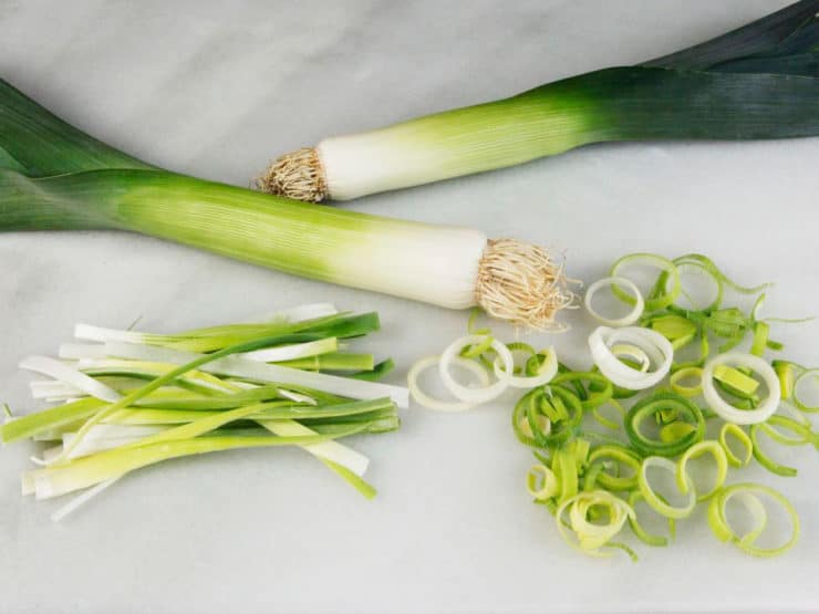 Horizontal shot - two leeks with julienne-cut and rings of leeks beside them on marble cutting board.