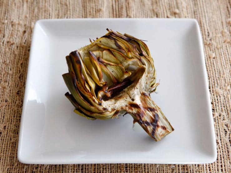 Grilled artichokes on a white square-shaped plate.