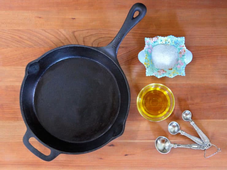 Clean seasoned cast iron pan on wooden background with oil, salt and measuring spoons on the side.