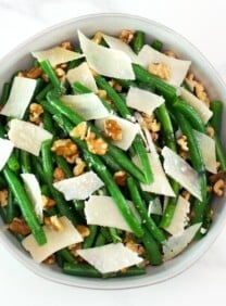 Green bean salad with walnuts and parmesan as garnish on a white bowl.