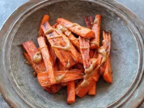 Horizontal shot of rustic tray of roasted carrots with tahini drizzle.