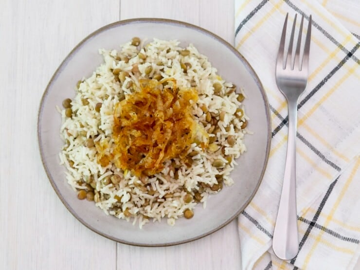 Overhead shot - small dish of lentils and rice - mujadara topped with caramelized onions, fork and cloth napkin on the side.