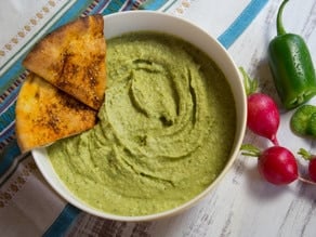 A zesty dip made with jalapeños, chickpeas, and spices in a white bowl with chips