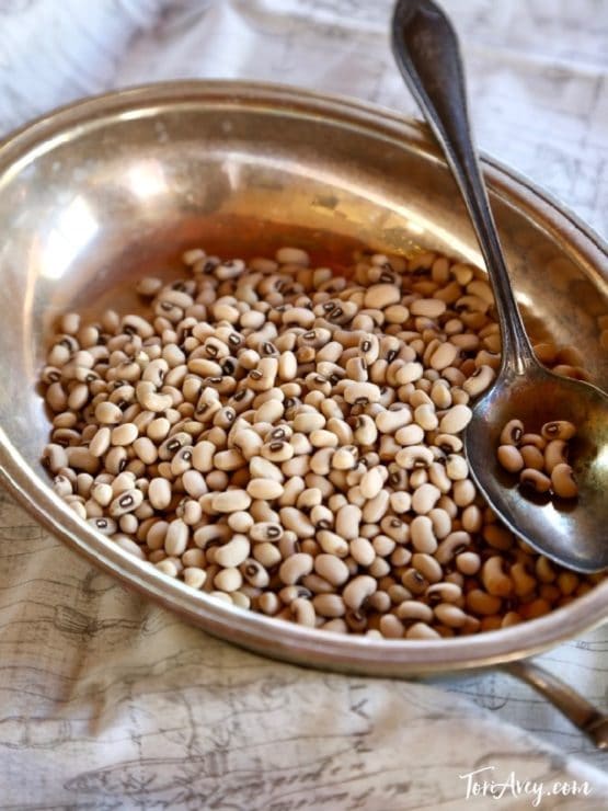 Metal dish of dried black eyed peas with a spoon on map cloth background.