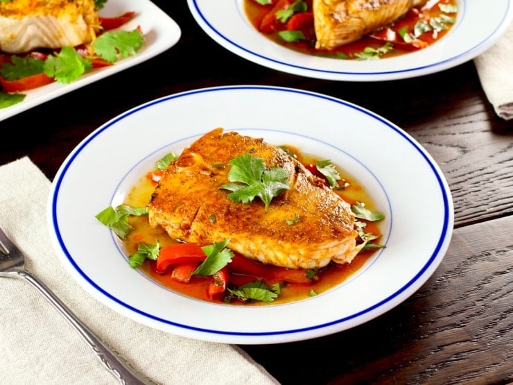 Moroccan paprika fish on a bed of vegetables topped wth fresh green herbs in a white bowl.