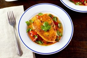 Moroccan paprika fish on a bed of vegetables topped wth fresh green herbs in a white bowl.