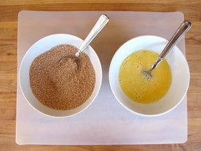 A bowl of breading and a bowl of whisked eggs.