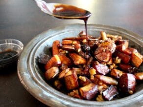 Spoon drizzling balsamic reduction onto roasted root vegetables and walnuts