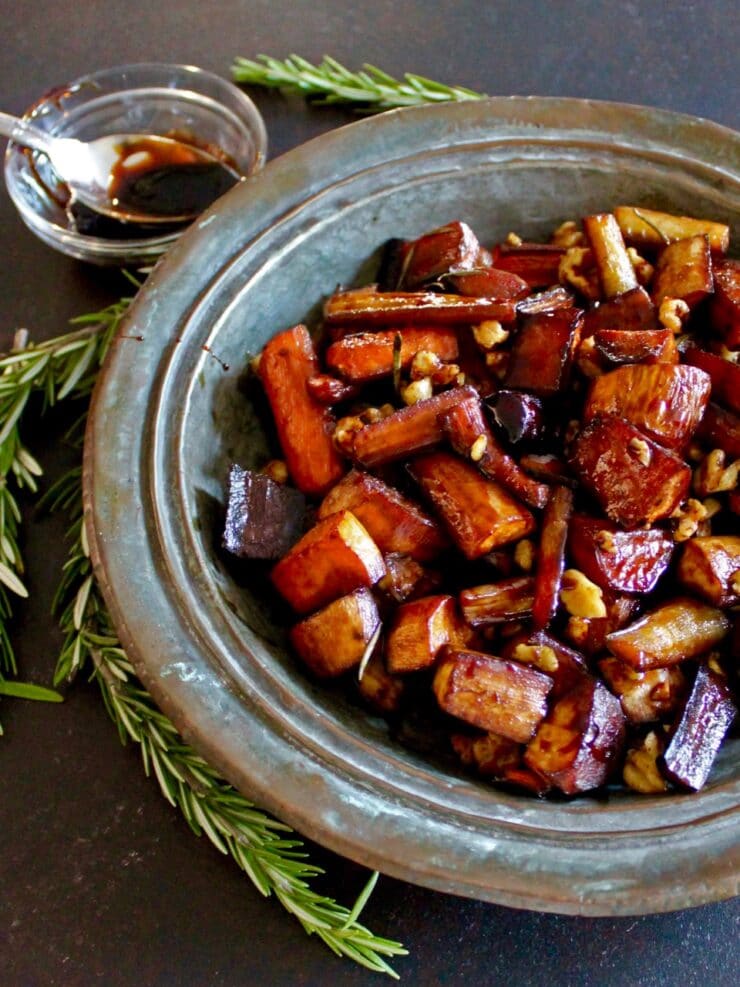 Roasted root vegetables on rustic metal platter, bowl of balsamic reduction in background, rosemary springs scattered around