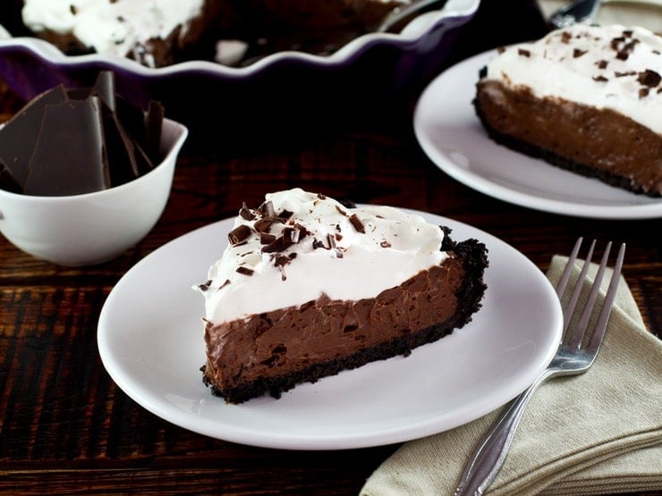 Slice of chocolate pie topped with whipped cream and chocolate shavings on a white plate.