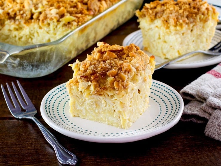 A square slice of kugel with a crunchy cookie topping on a white plate with a decorative border.