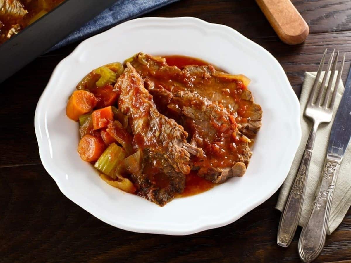 Overhead view of A slice of beef brisket next to a side of vegetables and topped with gravy on a round white plate.