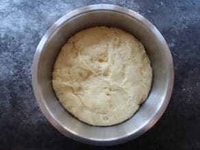 Raw sufganiyot dough in a large metal mixing bowl on top of a concrete surface.