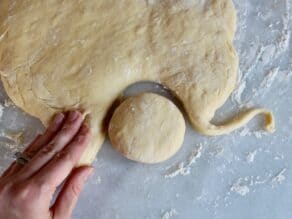 A circle of uncooked sufganiyot dough is cut out from a larger piece of dough.