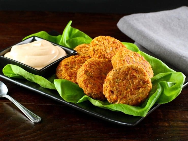 A serving platter filled with salmon cakes on a bed of lettuce next to a dish of spicy Sriracha sauce.