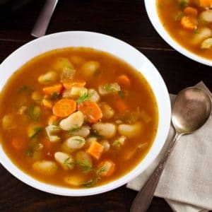 Overhead image of a bowl of butter bean soup in red broth in a white soup bowl next to a spoon.