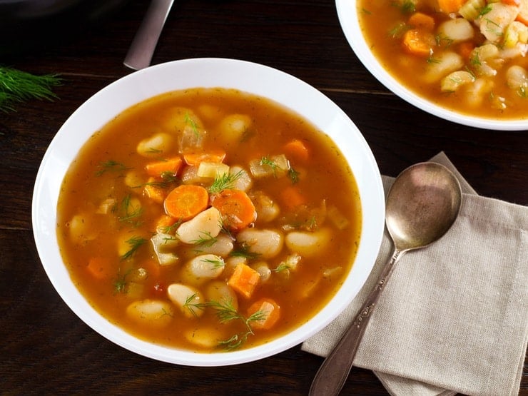 Overhead image of a bowl of butter bean soup in red broth in a white soup bowl next to a spoon.