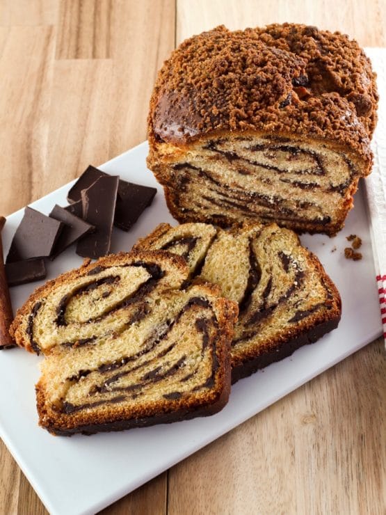 Overhead vertical shot of sliced chocolate babka with chocolate chunks on white cutting board with wood background.