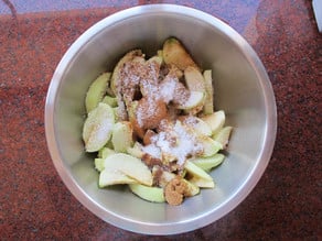 Sliced apples in a bowl, topped with sugar.