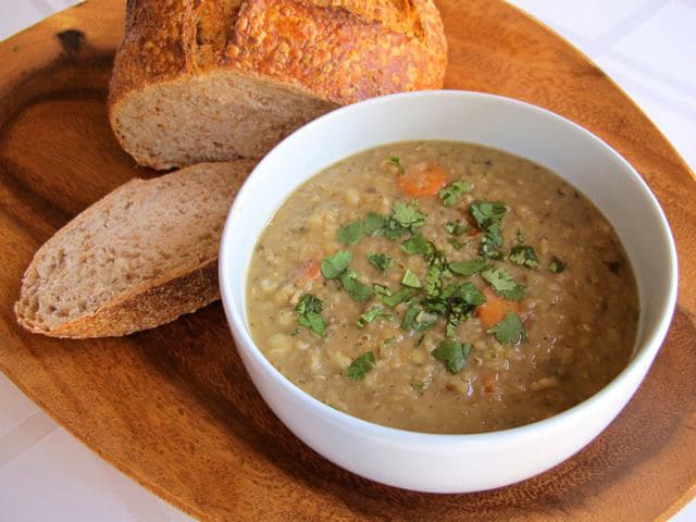 A bowl of lentil soup paired with a bread on a wooden plate