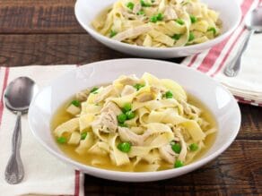 horizontal shot - bowl of chicken with homemade noodles and sweet peas with cloth napkin and spoon on wooden background.