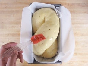 Brushing egg wash onto a risen loaf.