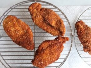 Fried golden schnitzels on rack with paper towels below.