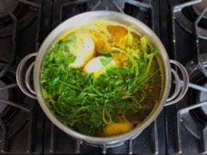 Soup stock cooking in large pot with onions and herbs.