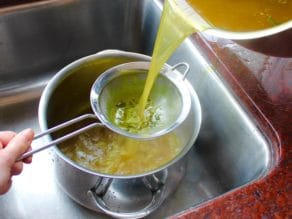 Soup stock is being poured through strainer into a large pot.