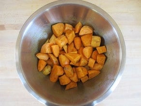 Potatoes tossed with seasoning in a mixing bowl.